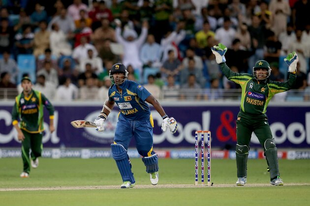 DUBAI, UNITED ARAB EMIRATES - DECEMBER 20:  Thisara Perera of Sri Lanka bats as Umar Akmal of Pakistan looks on during the second One-Day International (ODI ) match between Sri Lanka and Pakistan at the Dubai Sports City Cricket Stadium on December 20, 2013 in Dubai, United Arab Emirates.  (Photo by Francois Nel/Getty Images)