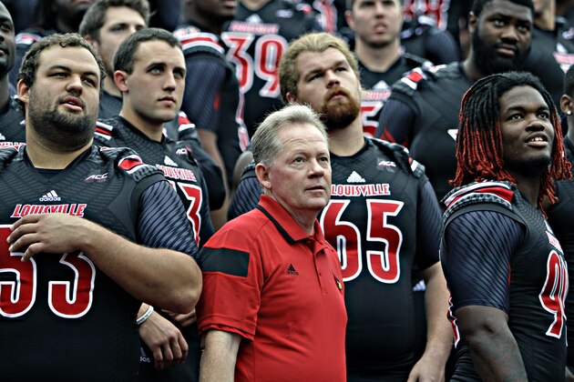 Louisville coach Bobby Petrino, center, and players Jake Smith, left, Brett Nelson (13), David Noltemeyer (65) and Lorenzo Mauldin, right, listen to instructions from the photographer as they prepare for the NCAA college football team photo on media day at Cardinal Stadium in Louisville, Ky., Saturday, Aug. 9, 2014.  (AP Photo/Garry Jones)
