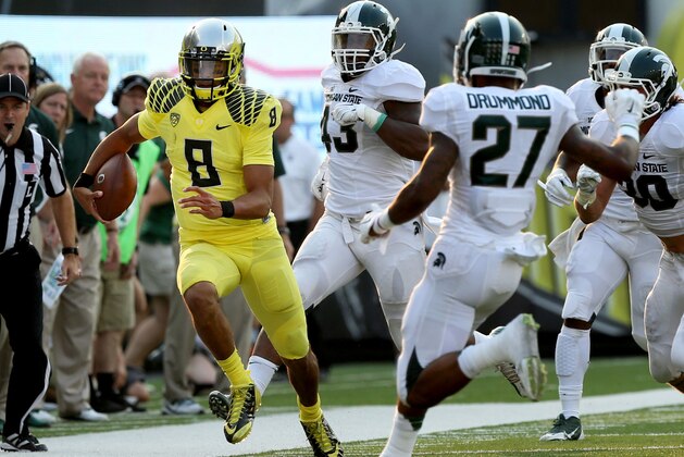 Oregon quarterback Marcus Mariota, left, runs down the sidelines ahead of a host of Michigan State defenders during the 3rd quarter of their NCAA college football game in Eugene, Oregon, Saturday Sept. 6, 2014. (AP Photo/Chris Pietsch)