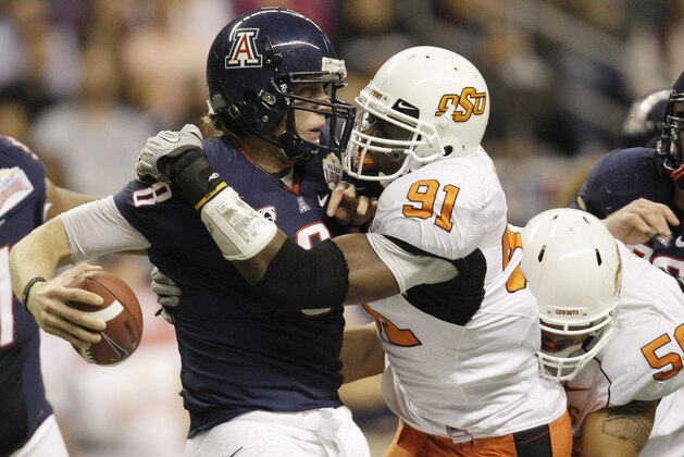 FILE - In this Dec. 29, 2010, file photo, Arizona's Nick Foles (8) is sacked by Oklahoma State's Ugo Chinasa (91) during the first quarter of the Alamo Bowl NCAA college football game, in San Antonio. Less than nine months after losing the Alamo Bowl 36-10 to Oklahoma State, the Wildcats get their chance at revenge against the ninth-ranked Cowboys on Thursday night, Sept. 8, 2011, at Boone Pickens Stadium. (AP Photo/Eric Gay, File)
