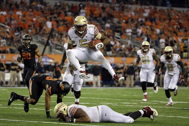 FILE - In this Aug. 30, 2014, file photo, Florida State quarterback Jameis Winston (5) leaps over guard Josue Matias, bottom, as Oklahoma State safety Jordan Sterns, left, is unable to stop Winston from reaching the end zone for a touchdown in the second half of an NCAA college football game in Arlington, Texas. hings didn't come nearly as easy for the Heisman winner, and the FSU offense will need to play much better if the Seminoles are to win the first College Football Playoff.  (AP Photo/Tony Gutierrez, File)