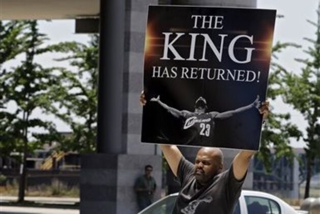 Graphic designer Alvin Smith holds up a poster in the street outside Quicken Loans Arena in Cleveland Friday, July 11, 2014, heralding the return of NBA basketball star LeBron James. James, who left the Cavaliers four years ago to join the Miami Heat, announced earlier he would return to the Cavaliers. (AP Photo/Mark Duncan) Graphic designer Alvin Smith holds up a poster in the street outside Quicken Loans Arena in Cleveland Friday, July 11, 2014, heralding the return of NBA basketball star LeBron James. James, who left the Cavaliers four years ago to join the Miami Heat, announced earlier he would return to the Cavaliers. (AP Photo/Mark Duncan)