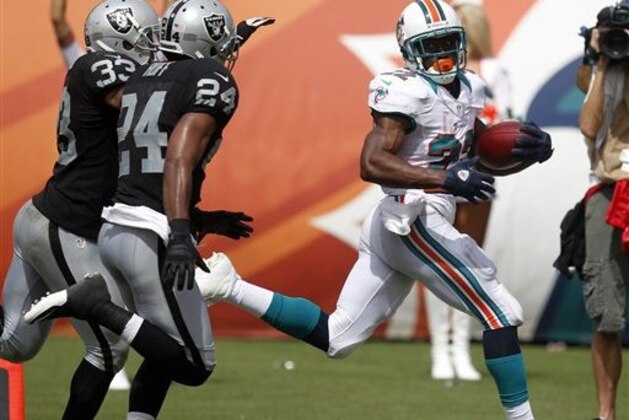 Miami Dolphins running back Reggie Bush (22) looks back toward Oakland Raiders free safety Michael Huff (24) and strong safety Tyvon Branch (33) while approaching the end zone during the second half of an NFL football game on Sunday, Sept. 16, 2012, in Miami. (AP Photo/Wilfredo Lee)