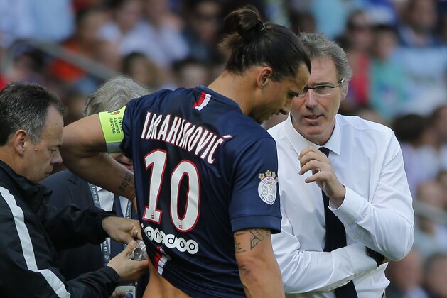 Paris Saint Germain's coach Laurent Blanc, right, talks to Swedish Zlatan Ibrahimovic, left, as he gets medical treatment after being injured, during a French League One soccer Match, Paris Saint Germain against Bastia, at Parc des Princes stadium, in Paris, Saturday, Aug. 16. 2014. Paris Saint Germain won 2-0. (AP Photo/Michel Euler)