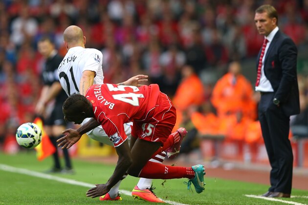 LIVERPOOL, ENGLAND - SEPTEMBER 13:  Mario Balotelli of Liverpool falls after a heavy challenge from Alan Hutton of Aston Villa as Brendan Rodgers looks on during the Barclays Premier League match between Liverpool and Aston Villa at Anfield on September 13, 2014 in Liverpool, England.  (Photo by Alex Livesey/Getty Images)