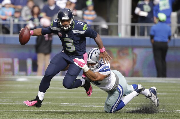 Seattle Seahawks quarterback Russell Wilson scrambles under pressure by Dallas Cowboys defensive end Tyrone Crawford in the first half of an NFL football game, Sunday, Oct. 12, 2014, in Seattle. (AP Photo/Elaine Thompson)