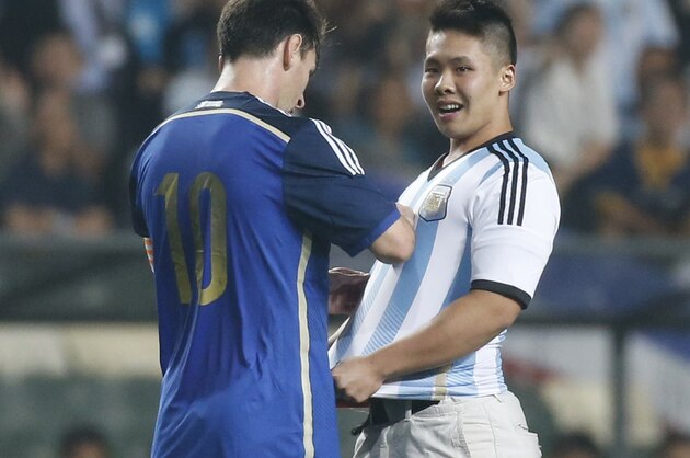 Argentina's Lionel Messi, left, signs an autograph for a supporter after the supporter ran onto the pitch past security officers during a friendly soccer match against Hong Kong in Hong Kong Tuesday, Oct. 14, 2014. (AP Photo/Kin Cheung)