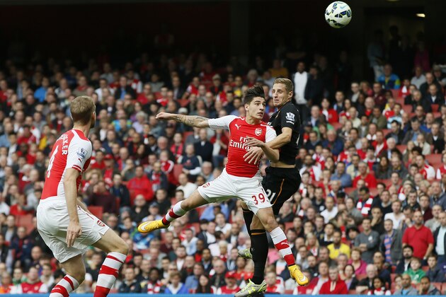 Arsenal's Hector Bellerin, center, jumps for the ball with Hull City’s Michael Dawson, right, during the English Premier League soccer match between Arsenal and Hull City at the Emirates stadium in London Saturday, Oct.18,  2014. (AP Photo/Alastair Grant)