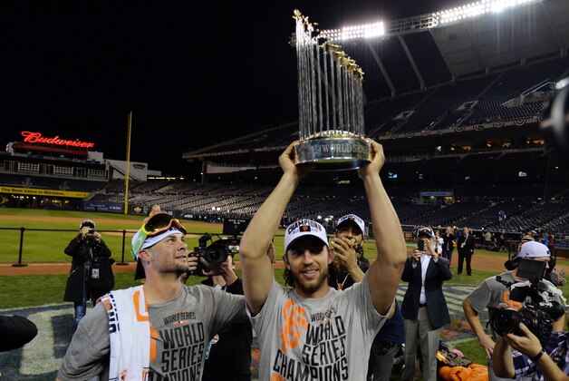 Oct 29, 2014; Kansas City, MO, USA; San Francisco Giants starting pitcher Ryan Vogelsong (left) watches as teammate Madison Bumgarner (middle) hoists the Commissioners Trophy after game seven of the 2014 World Series against the Kansas City Royals at Kauffman Stadium. Mandatory Credit: Peter G. Aiken-USA TODAY Sports