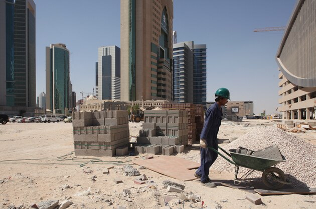 DOHA, QATAR - OCTOBER 23: (EDITORS NOTE: Image was created using a variable
planed lens.) A worker uses a wheelbarrow to move cinder blocks on a construction site in the budding new financial district on October 23, 2011 in Doha, Qatar. Qatar will host the 2022 FIFA World Cup football competition and is slated to tackle a variety of infrastructure projects, including the construction of new stadiums.  (Photo by Sean Gallup/Getty Images)