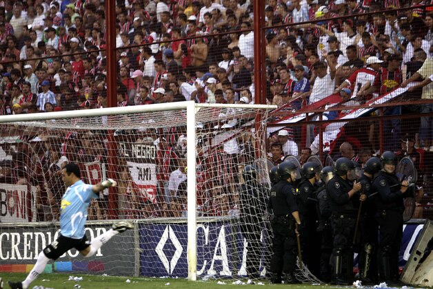 Chacarita Juniors' goalkeeper Nicolas Tauber, left,  kicks the ball as police officers stand guard in front of Chacarita Juniors' fans during an Argentinean soccer league match against Estudiantes de la Plata in Buenos Aires, Sunday May 2, 2010. (AP Photo/ Natacha Pisarenko)