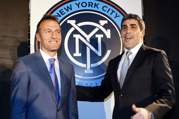 In this photo taken onMarch 20, 2014 and provided by New York City Football Club, New York City Football Club head coach Jason Kreis, left, and sporting director Claudio Reyna unveil the team's new team badge in New York. More than 100,000 votes were submitted online to select the badge. The New York City FC will begin Major League Soccer play in March of 2015. (AP Photo/New York City Football Club, Ray Stubblebine)