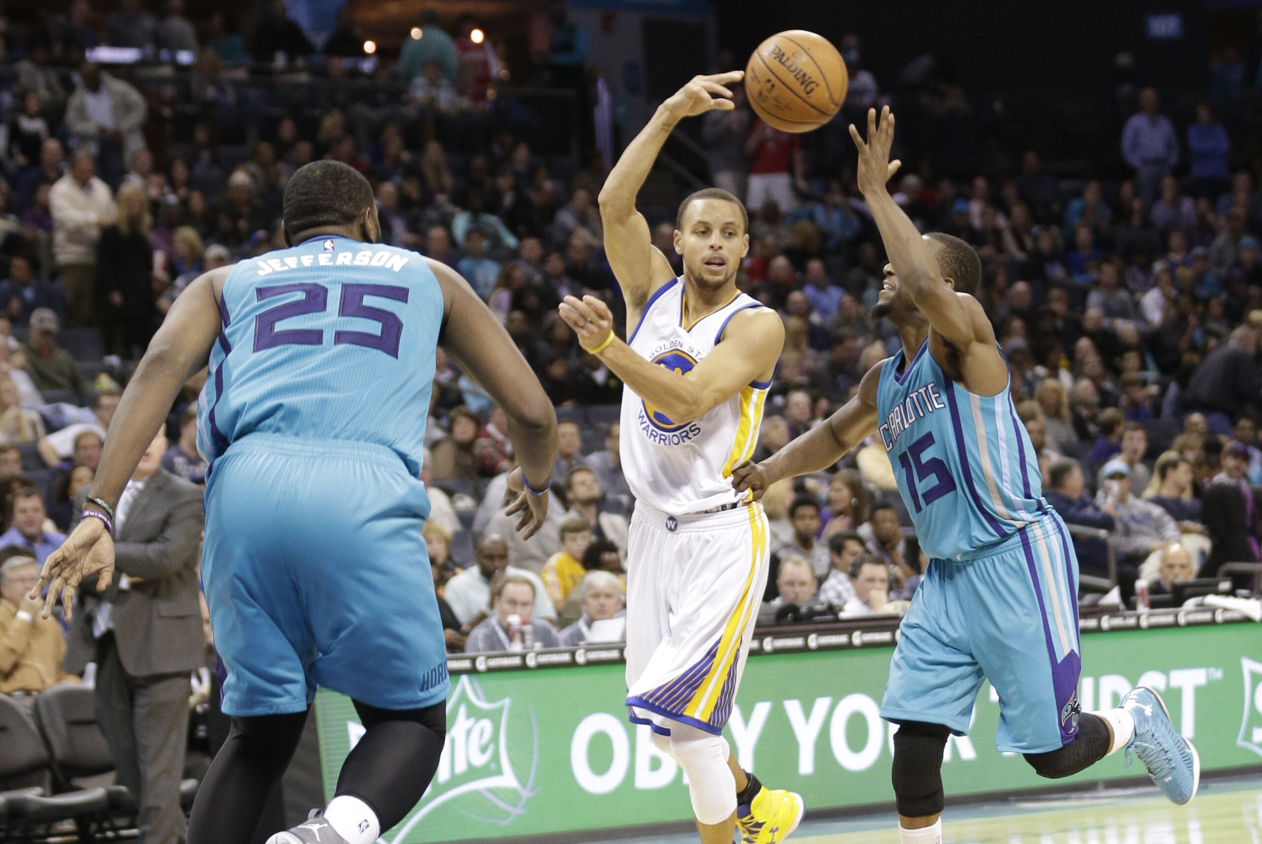 Golden State Warriors' Stephen Curry, center, passes the ball as he is guarded by Charlotte Hornets' Kemba Walker, right, and Al Jefferson, left, during the second half of an NBA basketball game in Charlotte, N.C., Friday, Nov. 28, 2014. The Warriors won 106-101. (AP Photo/Chuck Burton)