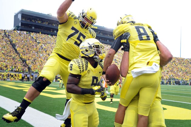 Oregon quarterback Marcus Mariota (8) is mobbed by teammates after scoring a touchdown during the second quarter of the NCAA college football game against the Tennessee in Eugene, Ore., Saturday, Sept. 14, 2013. (AP Photo/Steve Dykes)