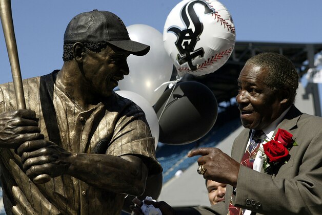 Minnie Minoso smiles in front of a sculpture of him before throwing out the ceremonial first pitch at U.S. Cellular Field prior to the game between the Chicago White Sox and Detroit Tigers Sunday, Sept. 19, 2004, in Chicago. The Chicago White Sox unveiled the life-sized sculpture to honor his role in the club's century-long history. (AP Photo/Nam Y. Huh)