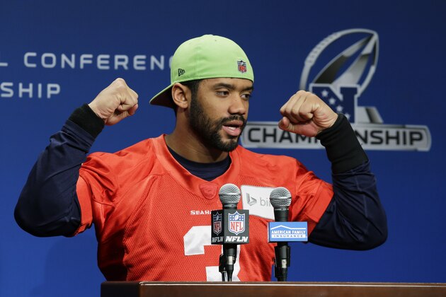 Seattle Seahawks quarterback Russell Wilson raises his arms and ends his remarks to reporters with his traditional