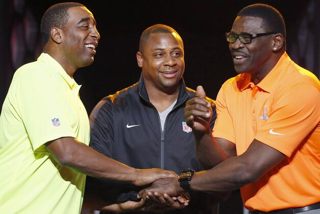 Troy Vincent, center, NFL Executive Vice President of Football Operations, smiles as he watches Michael Irvin, right, NFL Hall of Fame member and Pro Bowl Alumni captain, and Cris Carter, left, NFL Hall of Fame member and Pro Bowl Alumni captain, laugh as they battle for the coin toss on who gets to pick the first player  during the Pro Bowl Kickoff news conference Tuesday, Jan. 20, 2015, in Phoenix.  The upcoming NFL Pro Bowl football game will be played on Sunday. (AP Photo/Ross D. Franklin)