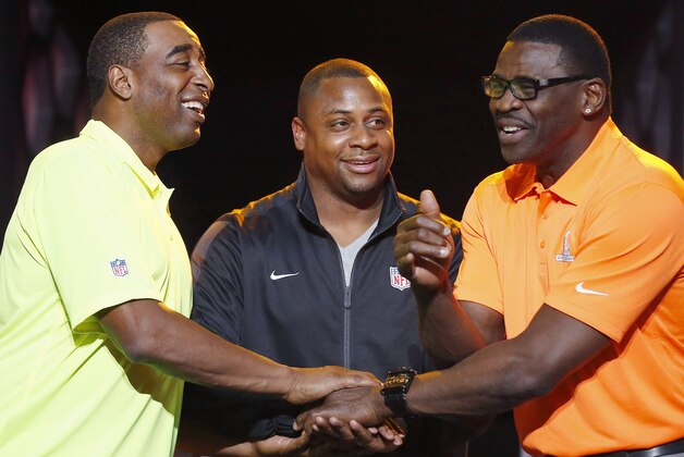 Troy Vincent, center, NFL Executive Vice President of Football Operations, smiles as he watches Michael Irvin, right, NFL Hall of Fame member and Pro Bowl Alumni captain, and Cris Carter, left, NFL Hall of Fame member and Pro Bowl Alumni captain, laugh as they battle for the coin toss on who gets to pick the first player  during the Pro Bowl Kickoff news conference Tuesday, Jan. 20, 2015, in Phoenix.  The upcoming NFL Pro Bowl football game will be played on Sunday. (AP Photo/Ross D. Franklin)
