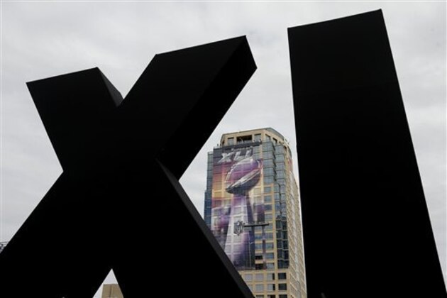 Framed by Roman numerals erected for Super Bowl XLIX, workers attach a sign to a building in downtown Phoenix Tuesday, Jan. 27, 2015. The New England Patriots face the Seattle Seahawks in Super Bowl XLIX on Sunday in Glendale, Ariz. (AP Photo/Charlie Riedel)