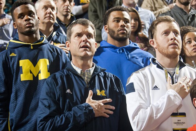 Michigan football head coach Jim Harbaugh, center, stands for the national anthem with son Jay, right, and recruits, before an NCAA college basketball game against Northwestern at Crisler Center in Ann Arbor, Mich., Saturday, Jan. 17, 2015. (AP Photo/Tony Ding)