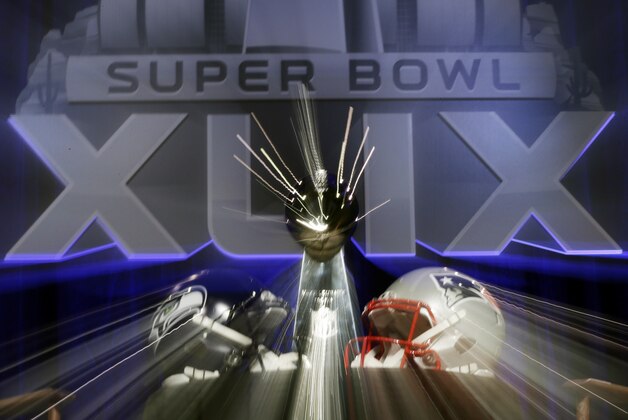In this photo taken with a slow shutter speed, the Lombardi Trophy sits behind two helmets before a joint coaches news conference for NFL Super Bowl XLIX football game Friday, Jan. 30, 2015, in Phoenix. (AP Photo/David J. Phillip)