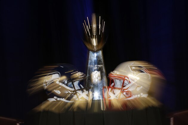 In this photo taken with a slow shutter speed, the Lombardi Trophy sits behind two helmets before a joint coaches news conference for NFL Super Bowl XLIX football game Friday, Jan. 30, 2015, in Phoenix. (AP Photo/Matt Slocum)