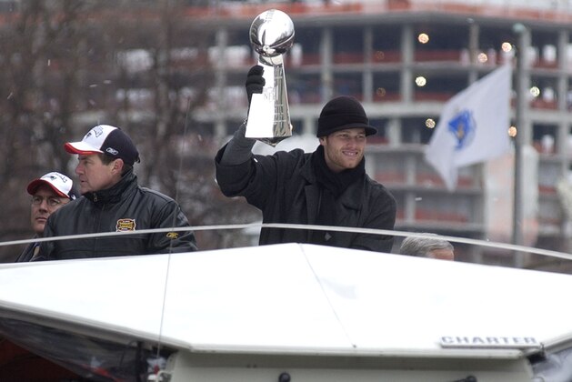 New England Patriots Tom Brady, MVP of Super Bowl XXXVIII, holds up the Super Bowl trophy as he rides in a parade celebrating the teams victory Tuesday, Feb 3, 2004 in Boston. Head coach Bill Belichick is at left. (AP Photo/Adam Hunger)