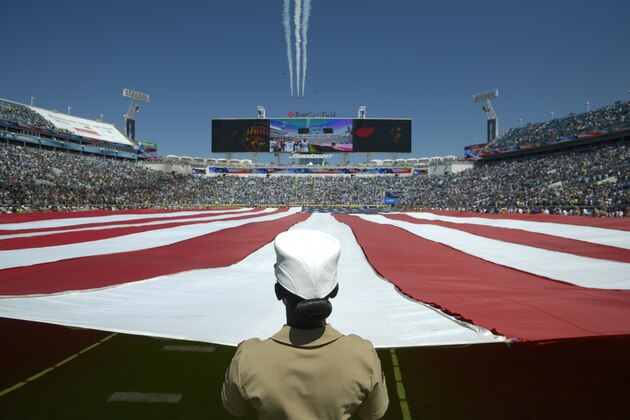 A member of the U.S. military helps hold a large American flag during a flyover before an NFL football game between the Jacksonville Jaguars and Indianapolis Colts in Jacksonville, Fla., Sunday, Sept. 21, 2014.(AP Photo/Phelan M. Ebenhack)