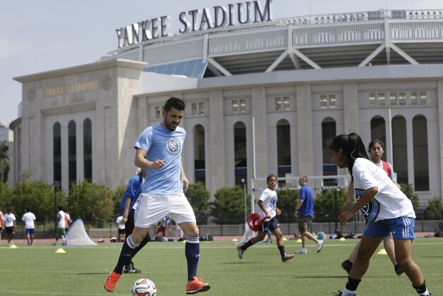 David Villa, left, plays soccer with kids from the South Bronx United program in front of Yankee Stadium in New York, Thursday, July 31, 2014. Villa, the Spanish all-time leading goal scorer, was the first player to sign with the New York City Football Club, which will be playing in the stadium. (AP Photo/Seth Wenig)