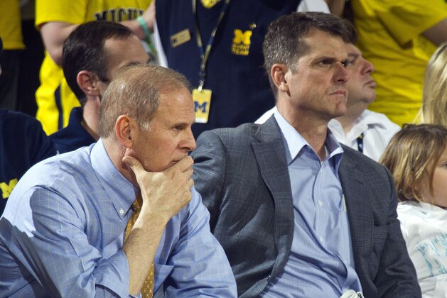 Michigan head coach John Beilein, left, sit next to Michigan football head coach Jim Harbaugh, center, in the first half of an NCAA college basketball game against Michigan State at Crisler Center in Ann Arbor, Mich., Tuesday, Feb. 17, 2015. (AP Photo/Tony Ding)