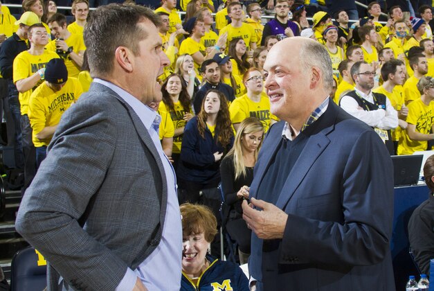 New Michigan football head coach Jim Harbaugh, left, speaks with Michigan interim athletic director Jim Hackett, right, before an NCAA college basketball game between Michigan and Michigan State at Crisler Center in Ann Arbor, Mich., Tuesday, Feb. 17, 2015. (AP Photo/Tony Ding)
