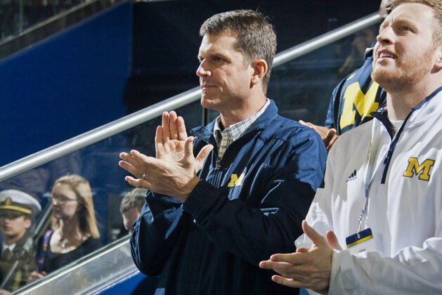 Michigan football head coach Jim Harbaugh, sitting with his son Jay, right, attends an NCAA college basketball game against Northwestern at Crisler Center in Ann Arbor, Mich., Saturday, Jan. 17, 2015. (AP Photo/Tony Ding)