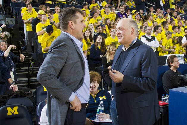 New Michigan football head coach Jim Harbaugh, left, speaks with Michigan interim athletic director Jim Hackett, right, before an NCAA college basketball game between Michigan and Michigan State at Crisler Center in Ann Arbor, Mich., Tuesday, Feb. 17, 2015. (AP Photo/Tony Ding)