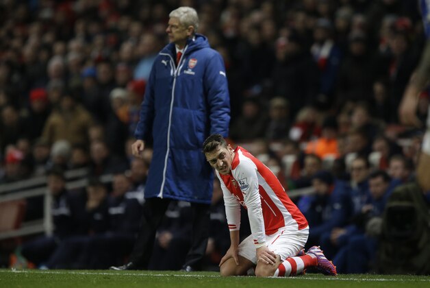 Arsenal's Mesut Ozil, right, kneels on the ground after a challenge, backdropped by his French manager Arsene Wenger, during the English Premier League soccer match between Arsenal and Leicester City at the Emirates Stadium in London, Tuesday, Feb. 10, 2015.  (AP Photo/Matt Dunham)