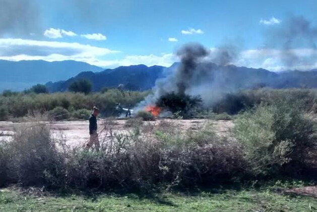 A man stands near the smoking remains of a helicopter that crashed with another near Villa Castelli in the La Rioja province of Argentina, Monday, March 9, 2015. Two helicopters carrying passengers filming the popular European reality show “Dropped” crashed Monday in a remote area of northwest Argentina, killing everyone on board, authorities said. (AP Photo/Gabriel Gonzalez)