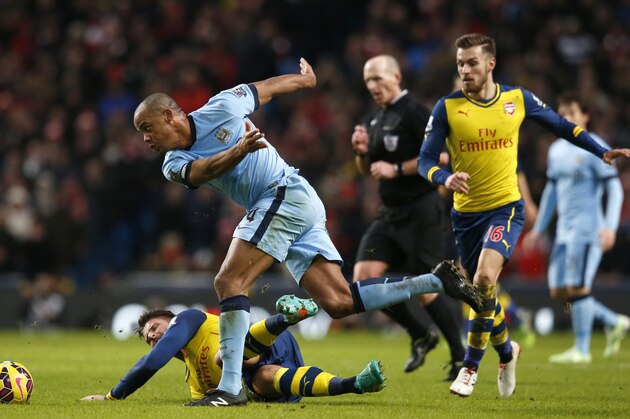 Manchester City's Vincent Kompany, centre, fouls Arsenal's Olivier Giroud for which he is shown a yellow card during the English Premier League soccer match between Manchester City and Arsenal at the Etihad Stadium, Manchester, England, Sunday, Jan. 18, 2015. (AP Photo/Jon Super)