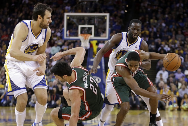 Milwaukee Bucks' Brandon Knight, right, drives the ball past Golden State Warriors' Draymond Green during the second half of an NBA basketball game Thursday, March 20, 2014, in Oakland, Calif. At left are Warriors' Andrew Bogut (12) and Bucks' Zaza Pachulia (27). (AP Photo/Ben Margot)
