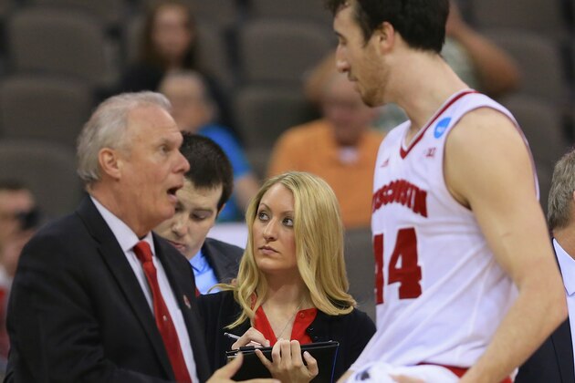 In this photo from March 20, 2015, Kat Vosters, director of basketball operations for men's basketball, stands between Wisconsin coach Bo Ryan, left, and Frank Kaminsky (44) during the second half of an NCAA tournament college basketball game against Coastal Carolina in the Round of 64 in Omaha, Neb. Vosters grew up in Wisconsin, graduated from Wisconsin, has been a Badgers fan since basically birth. (AP Photo/Nati Harnik)