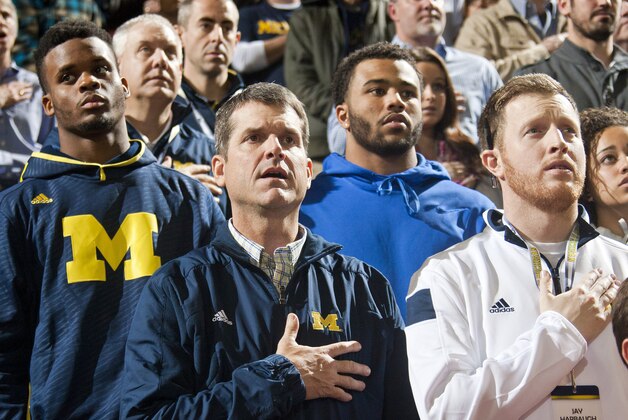 Michigan football head coach Jim Harbaugh, center, stands for the national anthem with son Jay, right, and recruits, before an NCAA college basketball game against Northwestern at Crisler Center in Ann Arbor, Mich., Saturday, Jan. 17, 2015. (AP Photo/Tony Ding)