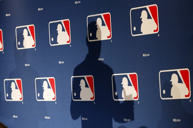 The shadow of MLB Commissioner Rob Manfred falls on a MLB logo backdrop, as Manfred talks about new rules aimed at speeding up play of baseball games among other major topics of conversation at spring training media day Monday, Feb. 23, 2015, in Phoenix.  (AP Photo/Ross D. Franklin)