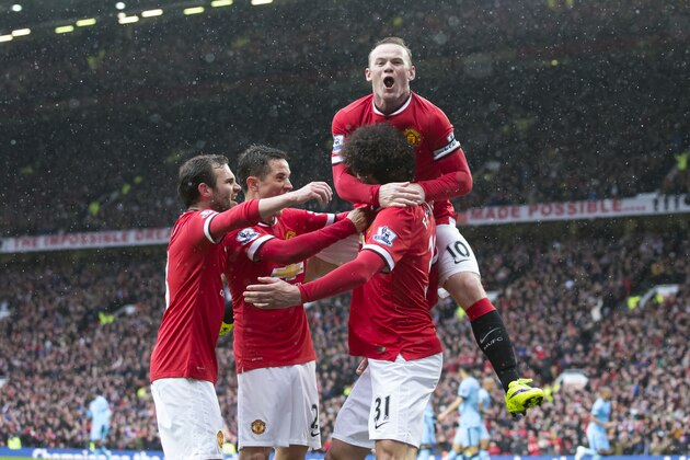 Manchester United's Marouane Fellaini, bottom right, celebrates with teammates including captain Wayne Rooney, top, after scoring during the English Premier League soccer match between Manchester United and Manchester City at Old Trafford Stadium, Manchester, England, Sunday, April 12, 2015. (AP Photo/Jon Super)