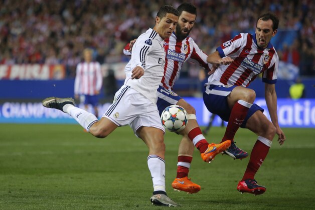Real Madrid's Cristiano Ronaldo fights for the ball against Atletico's Diego Godin and Atletico's Arda Turan during the Champions League quarterfinal first leg soccer match between Atletico Madrid and Real Madrid at the Vicente Calderon stadium in Madrid, Spain, Tuesday, April 14, 2015. (AP Photo/Andres Kudacki)
