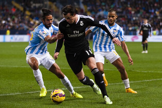Real Madrid's Gareth Bale from Wales, center, duels for the ball against Marcos Alberto Angeleri from Argentina, left, and Roberto Jose Rosales from Venezuela, right, during a Spanish La Liga soccer match between Malaga and Real Madrid at La Rosaleda stadium in Malaga, Spain, Saturday Nov. 29, 2014. (AP Photo/Daniel Tejedor)