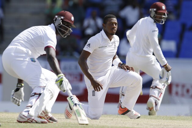 England's bowler Chris Jordan kneels as West Indies' Jason Holder, left, and Denesh Ramdin, turn to run, during the last day of their first cricket Test match at the Sir Vivian Richards Cricket Ground in Antigua, Antigua and Barbuda, Friday, April 17, 2015.  (AP Photo/Ricardo Mazalan)