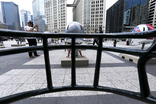 A tourist poses for a photo under a replica NFL Dallas Cowboys football helmet, as viewed through another helmet on display in Pioneer Court, Friday, April 17, 2015, in downtown Chicago as the city prepares to host the NFL Draft from April 30 to May 2. (AP Photo/Charles Rex Arbogast)
