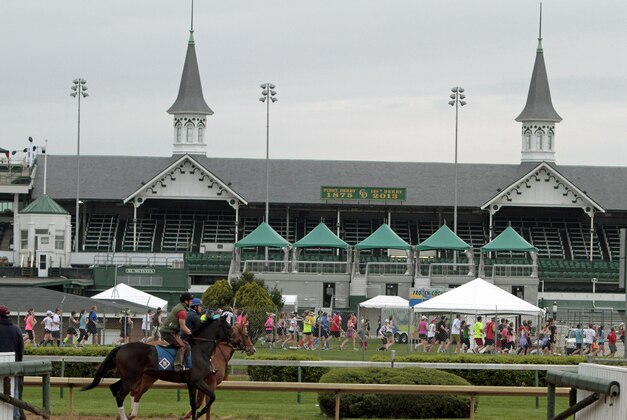 As thoroughbreds train on the main track at Churchill Downs Saturday, April 27, 2013 in Louisville, Ky., runners in the Kentucky Derby Festival mini marathon and marathon race through the infield and back out of the historic race track. (AP Photo/Garry Jones)