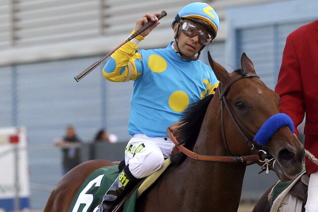 Victor Espinoza raises his whip as he and American Pharoah are led to the Winner's Circle after the Arkansas Derby horse race at Oaklawn Park in Hot Springs, Ark., Saturday, April 11, 2015. (AP Photo/Danny Johnston)
