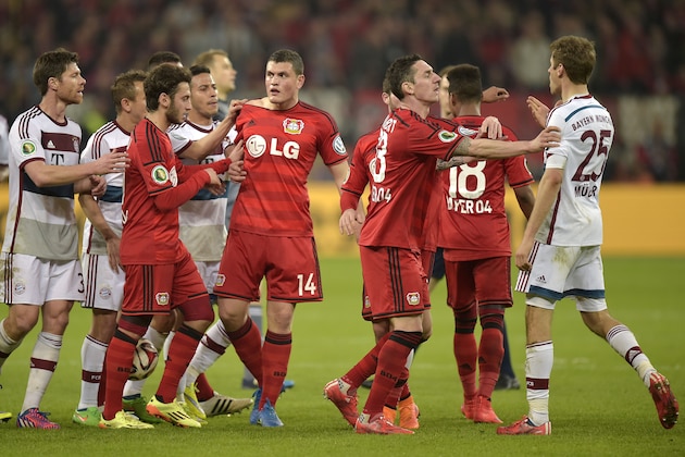 Leverkusen's Kyriakos Papadopoulos from Greece, center, and Bayern's Thomas Mueller are hold back after they argued during a German soccer cup quarter final match between Bayer 04 Leverkusen and Bayern Munich in Leverkusen, western Germany, Wednesday, April 8, 2015. (AP Photo/Martin Meissner)