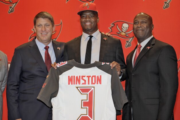 Tampa Bay Buccaneers first-round draft pick Jameis Winston, center, holds his jersey as he stands with general manager Jason Licht, left, and head coach Lovie Smith, right, during a news conference Friday, May 1, 2015, in Tampa, Fla. Winston, a former Florida State quarterback, was the first overall pick. (AP Photo/Chris O'Meara)