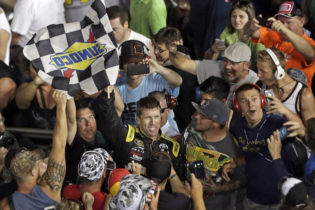 Carl Edwards waves the checkered flag as he celebrates with fans after winning the NASCAR Sprint Cup series auto race at Charlotte Motor Speedway in Concord, N.C., Sunday, May 24, 2015. (AP Photo/Gerry Broome)